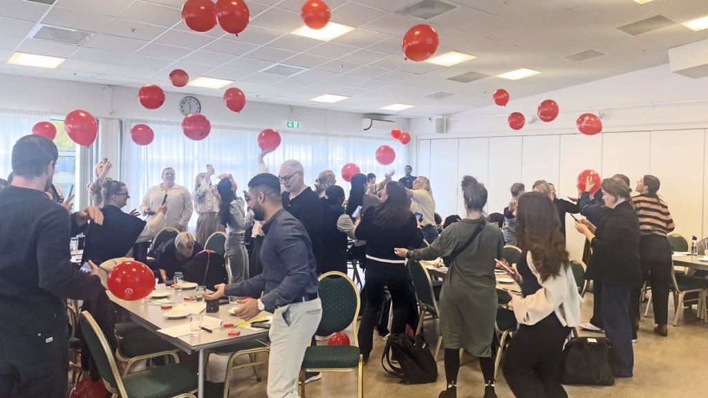 En sal myllrar av liv när alla deltagare i utbildningen gör en övning. I luften studsar massor av röda ballonger runt.