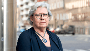 Åse har kort, grått hår och bär glasögon.