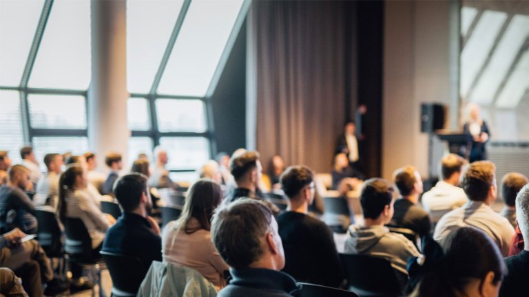 Flera personer sitter i en stor mötessal.