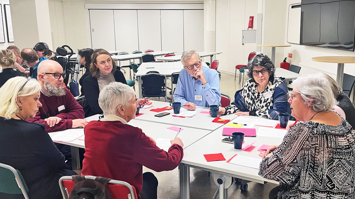 En grupp på åtta personer sitter tillsammans och diskuterar. Bakon dem skymtar en annan grupp.