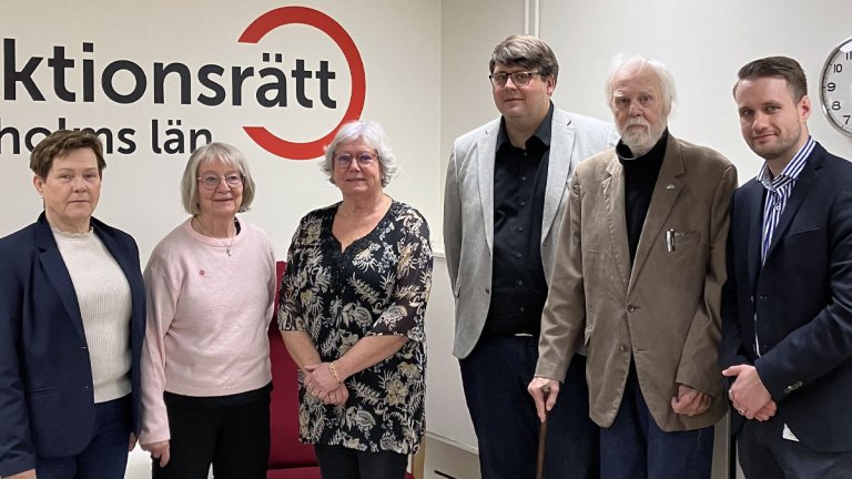 Vårt presidium och tre representanter från Sverigedemokraterna står framför en vägg med Funktionsrätt Stockholms läns logga.
