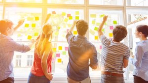 En grupp personer står framför ett stort fönster och sätter upp olikfärgade postit-lappar.