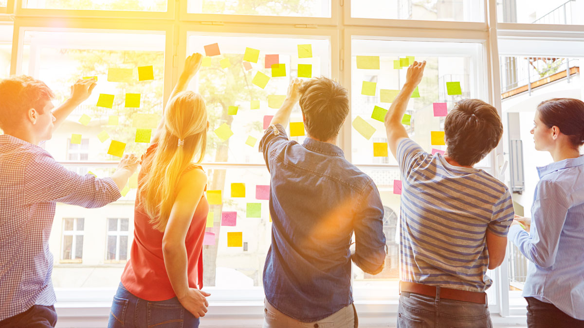 En grupp personer står framför ett stort fönster och sätter upp olikfärgade postit-lappar.