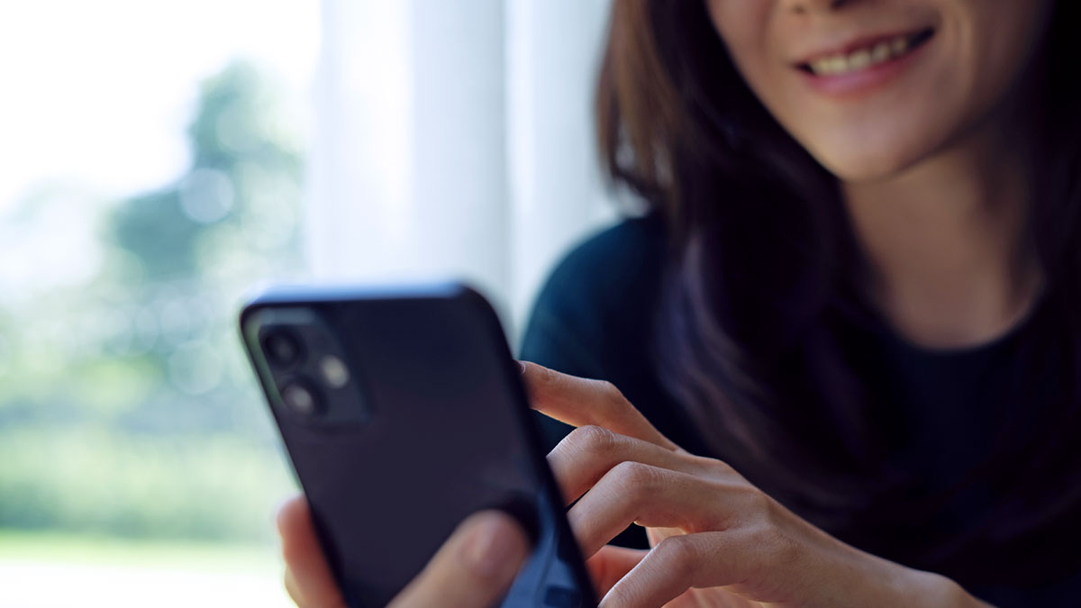 En leende kvinna slår ett nummer på sin telefon.