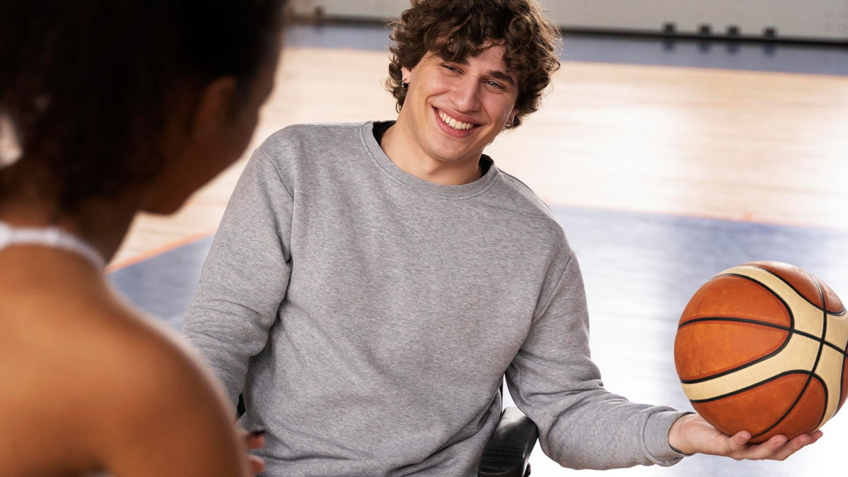 En kille och en tjej spelar rullstolsbasket. Killen håller i bollen, han ser glad ut.