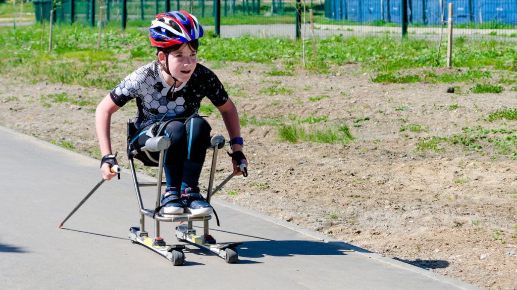 En pojke åker rullskidor sittandes i ett hjälpmedel .Han ser fokuserad ut.
