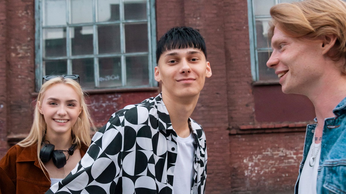 Tre ungdomar rör sig utanför en äldre byggnad. Alla tre ser glada ut.