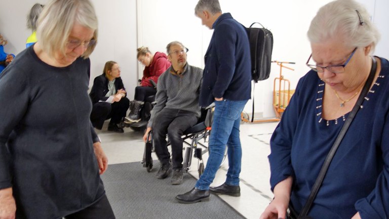 Samverkansgruppen är samlade på och omkring en grå torkmatta. Många riktar blicken nedåt.