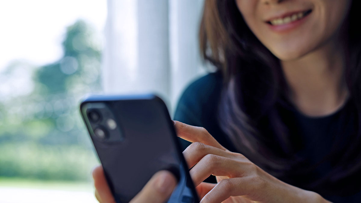 En leende kvinna slår ett nummer på sin telefon.