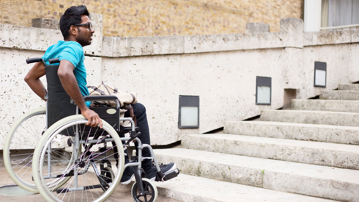 En ung kille i rullstol tittar upp mot trappan framför sig. Han ser frustrerad ut.