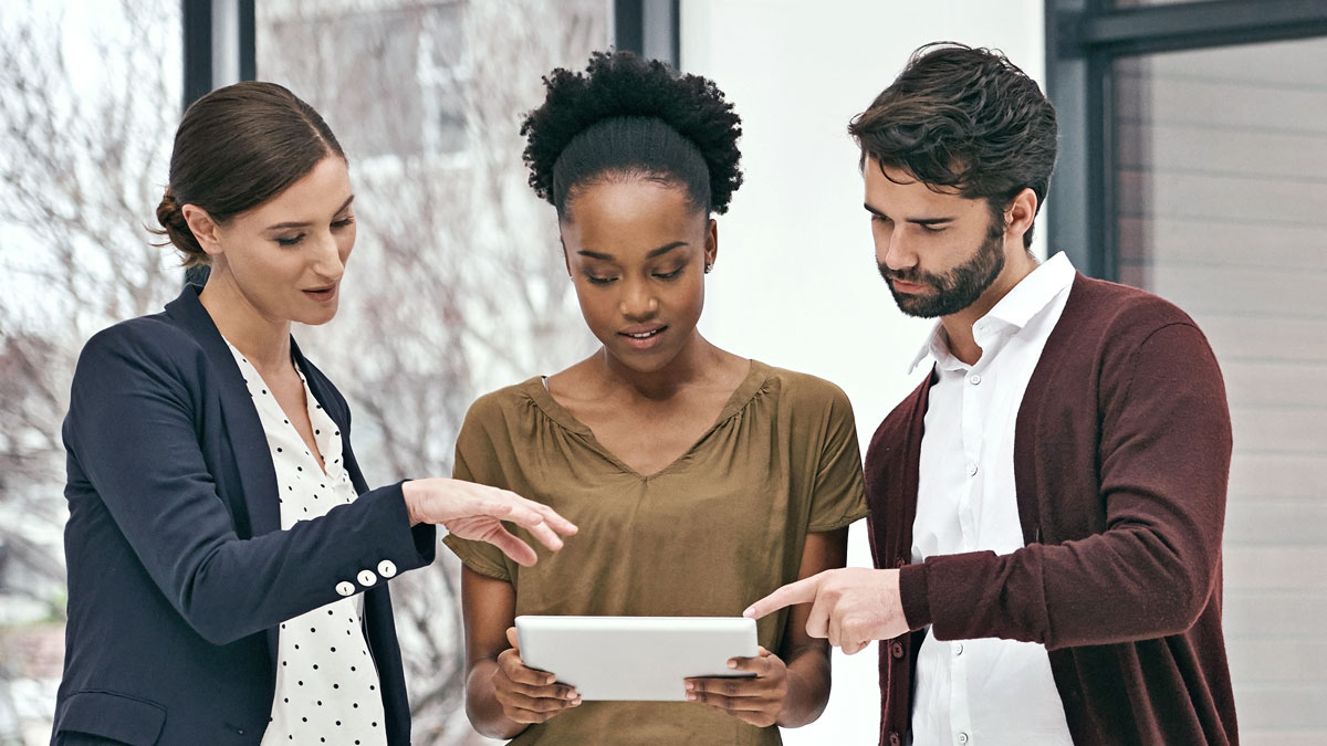 Tre personer tittar fokuserat på något på en läsplatta, som en av dem håller i.