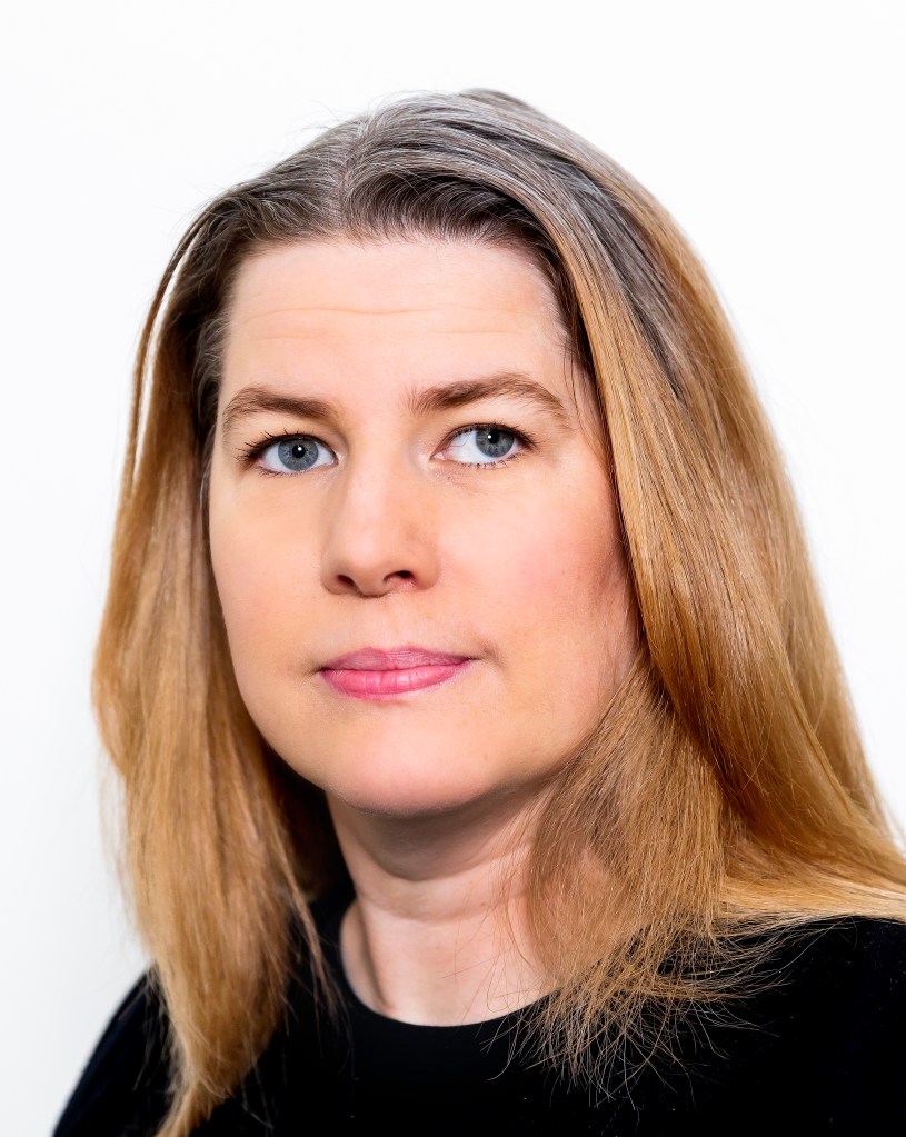 Åsa har ljusbrunt hår och blå ögon. Hon ser allvarlig ut.