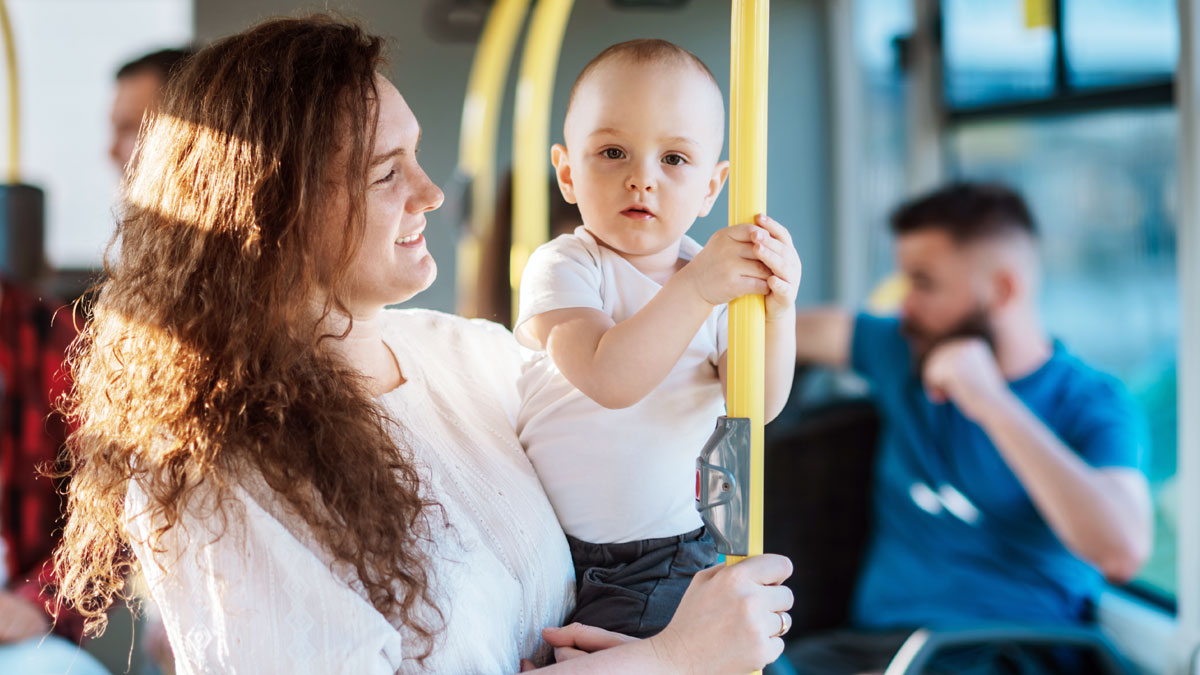 En leende kvinna håller ett barn i famnen. De är på en buss. Barn är ett av våra temaår.