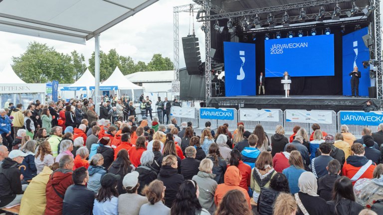 En politiker står på Järvaveckans stora scen, framför en stor folksamling. Vi vill göra gemensam sak på Järvaveckan!