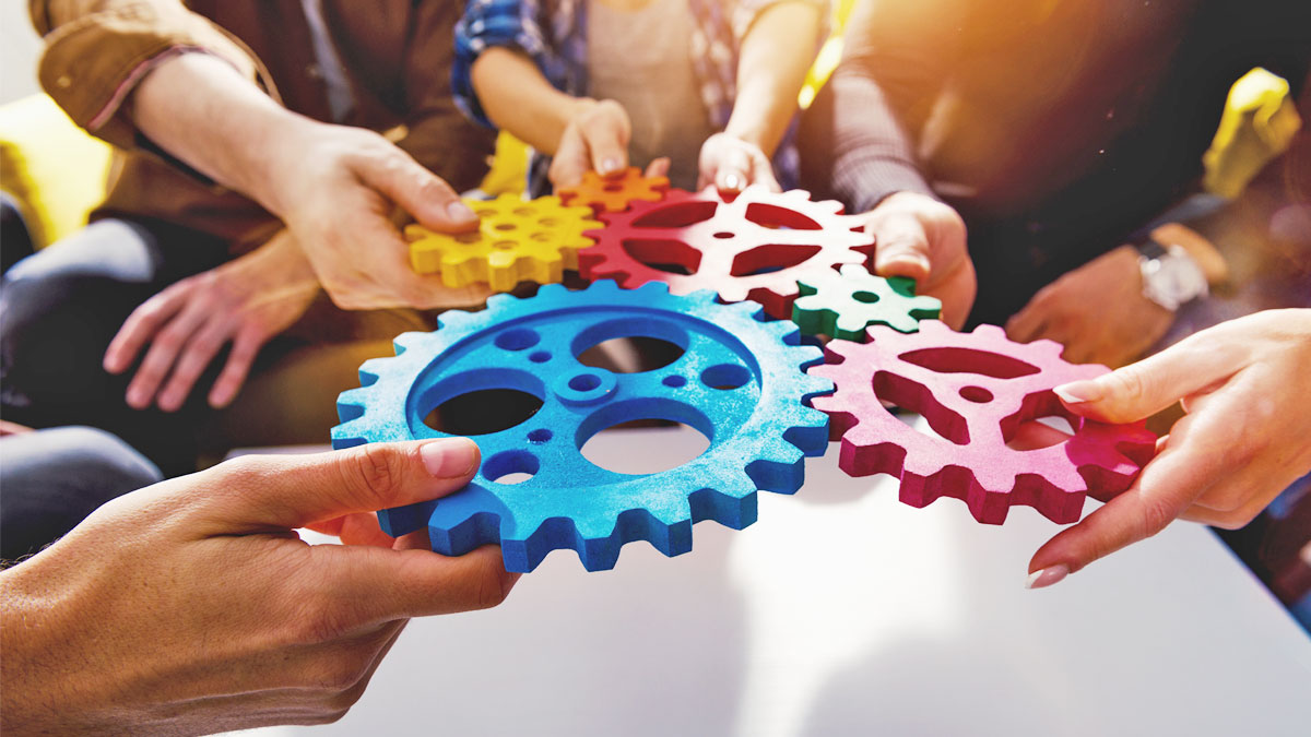 Händerna på flera personer som räcker fram kugghjul i olika färger och storlekar, för att symbolisera intressepolitik.