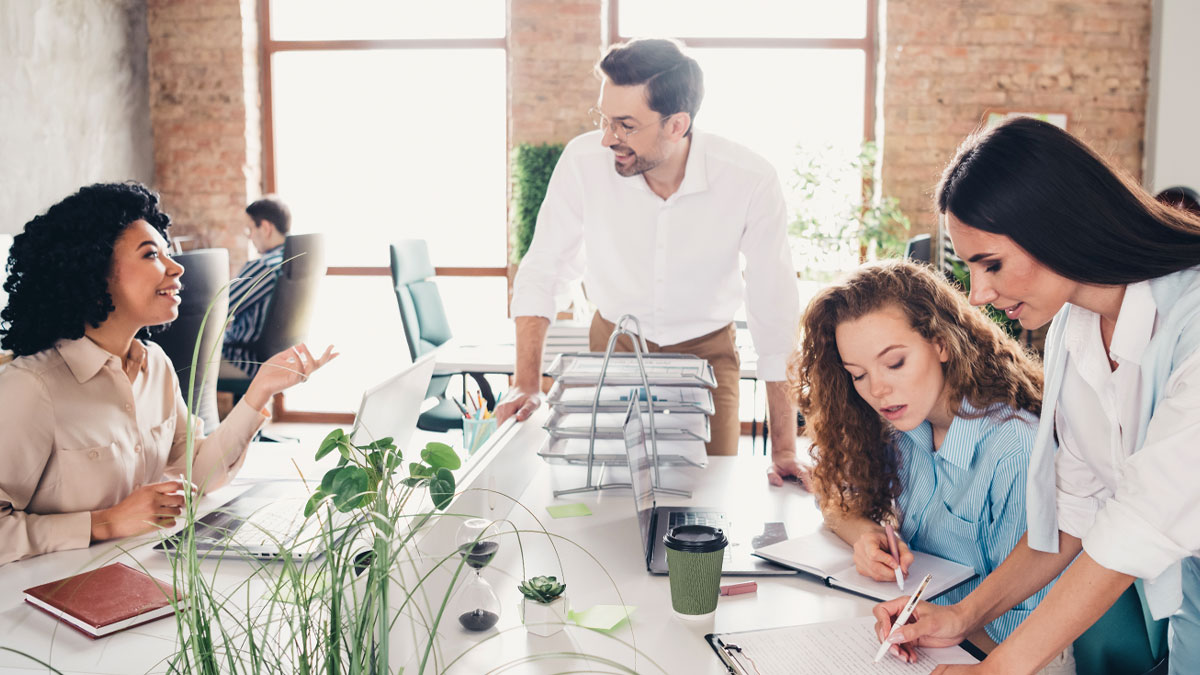 Två spontanmöten i ett luftigt kontorslandskap. En kvinna och en man pratar leendes. Två kvinnor mittemot fokuserar på ett dokument.