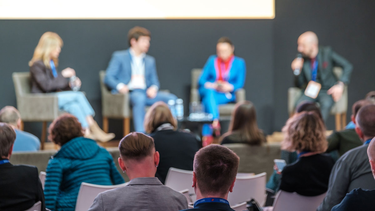 I förgrunden en publik bakifrån. Lite suddiga i bakgrunden sitter fyra regionpolitiker på en scen och diskuterar.