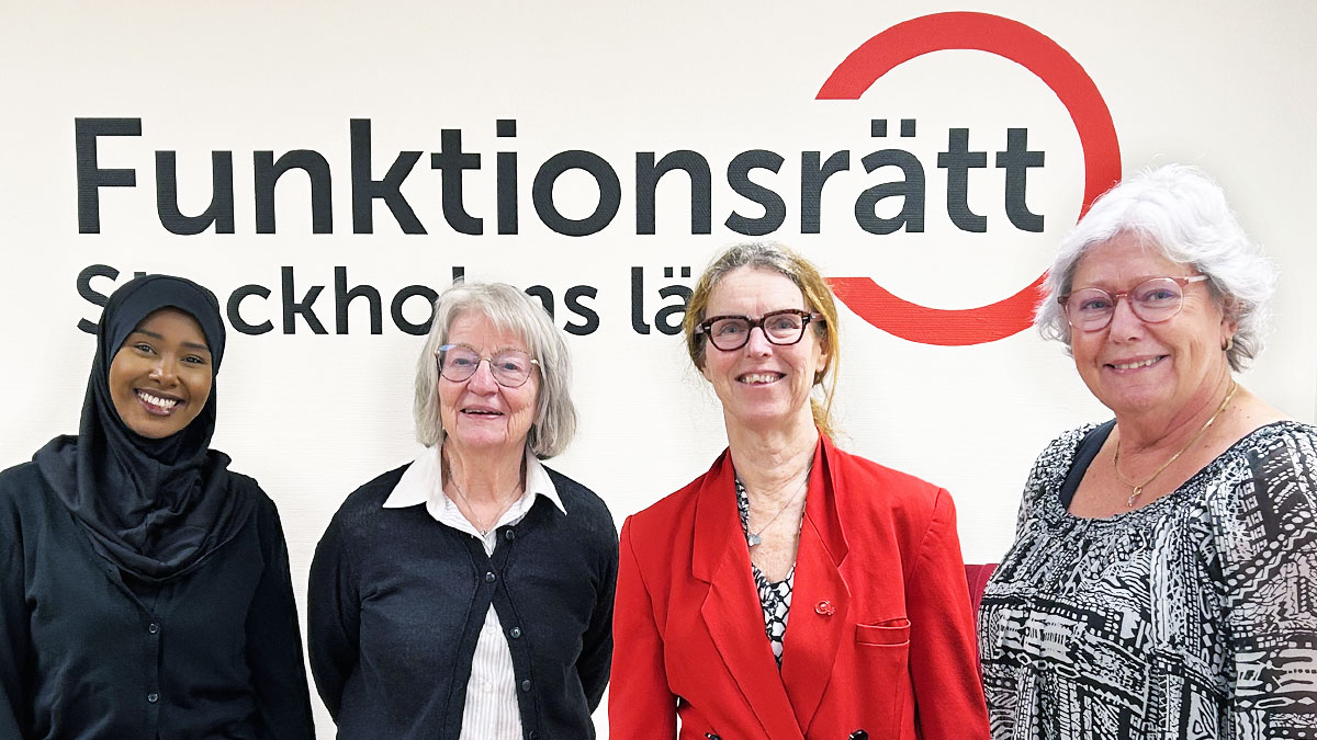 Fyra personer står på rad framför en vägg med Funktionsrätt Stockholms läns logga. De ler mot kameran.