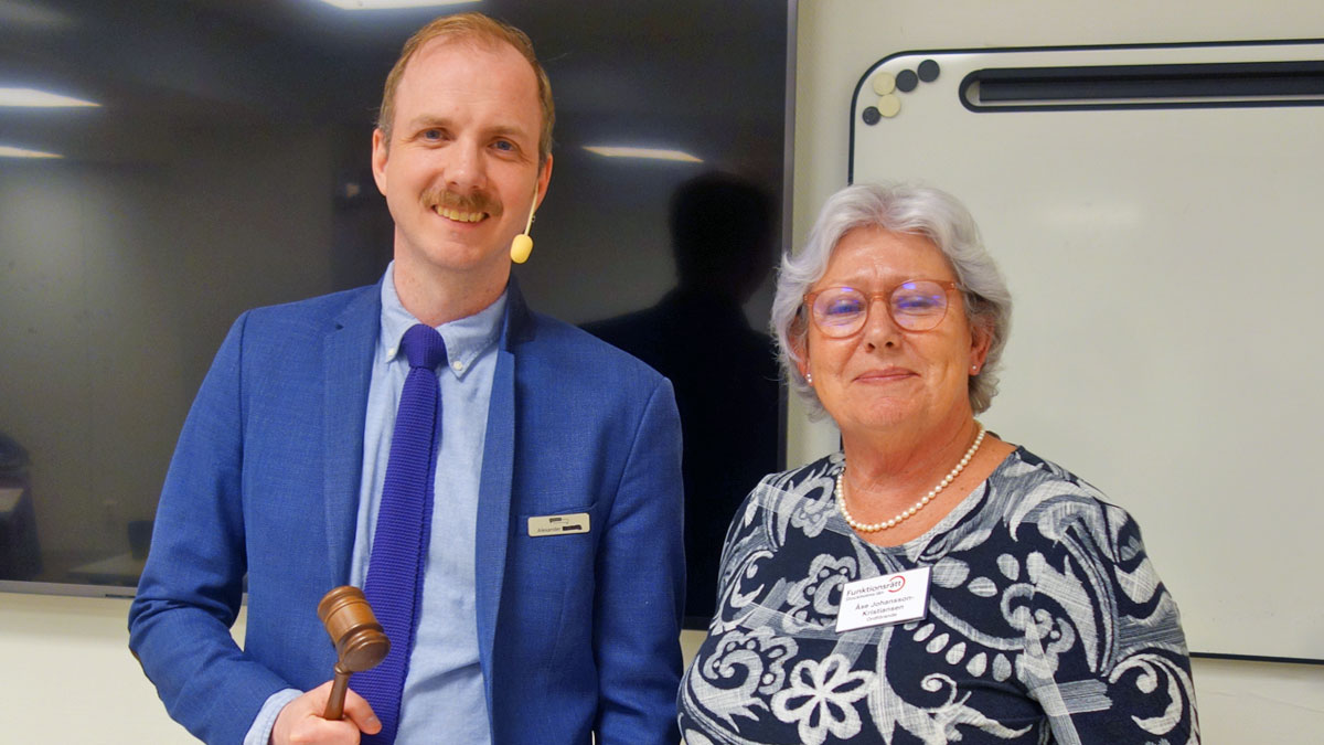Alexander Dagh, årsmötesorförande, och Åse, ordförande för Funktionsrätt Stockholms län, står tillsammans. Alexander håller upp ordförandeklubban. Båda ler.