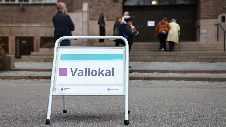 En skylt med texten vallokal. Bakom den går flera personer upp för en trappa och in i vallokalen.
