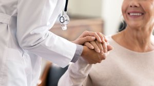 En läkare håller en patients hand mellan sina egna händer. Patienten ler stort.
